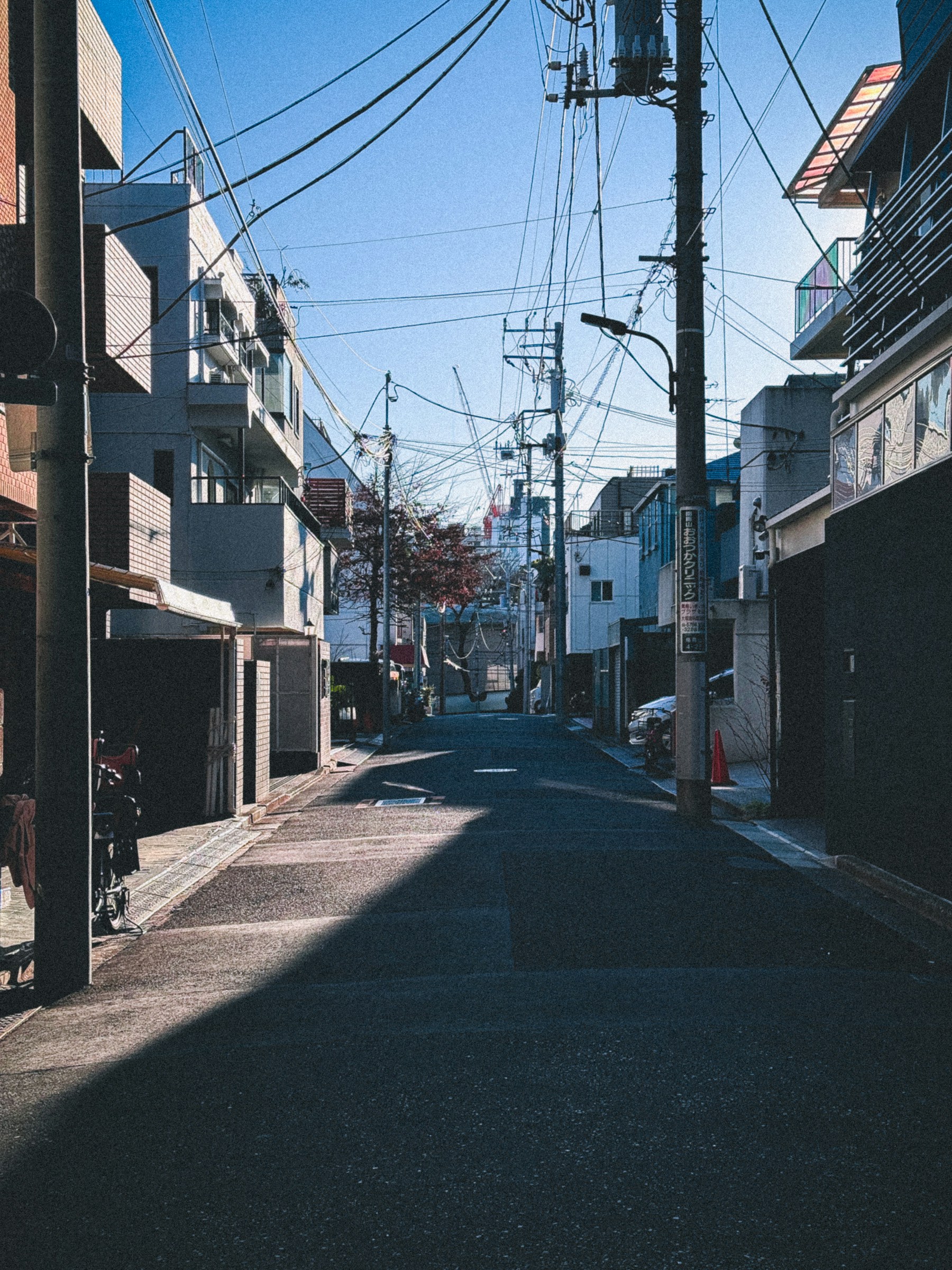 Sunlight along a quiet neighborhood street in Tokyo, with small shops and overhead wires